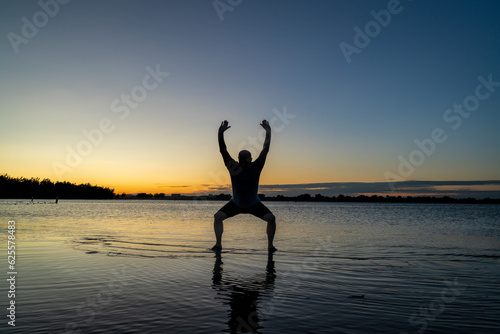 sunrise silhouette of a man standing in shallow water and practicing chigong or tai chi movements, Boyd Lake State Park in northern Colorado