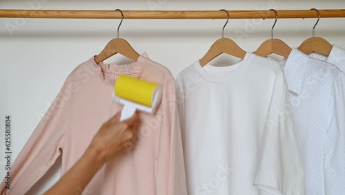 A woman's hand cleans clothes with a reusable clothes roller hanging on a wooden hanger.