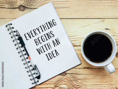 Open notebook with text "Everything begins with an idea" and a cup of coffee on wooden background.