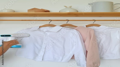 An unrecognizable woman steams a t-shirt hanging on a wooden hanger
