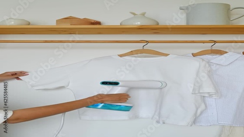 An unrecognizable woman steams a t-shirt hanging on a wooden hanger