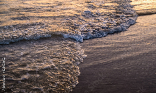 The oncoming wave in the blur in the sunset light. Background of water trail in long exposure with white foamy splashes.