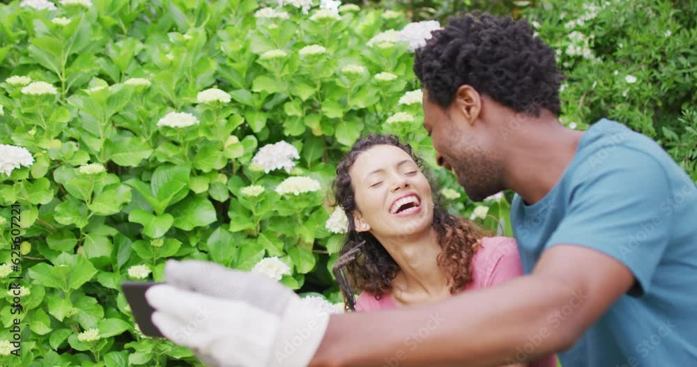 Happy biracial couple gardening together, taking selfie with flowers Happy biracial couple gardening together, taking selfie with flowers