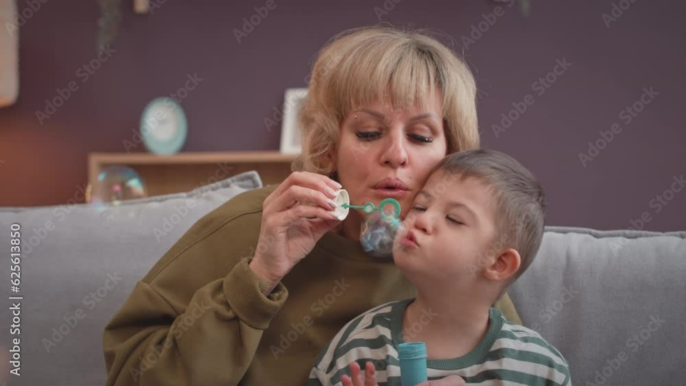 Waist up of happy 6 year old Caucasian boy with down syndrome and his beloved mother blowing soap bubbles in living room together Waist up of happy 6 year old Caucasian boy with down syndrome and his beloved mother blowing soap bubbles in living room together
