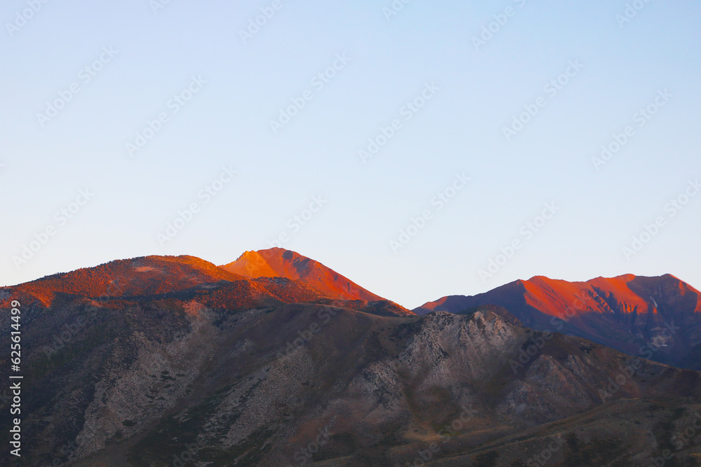 The peaks of the mountains are illuminated by the setting light of the sun.