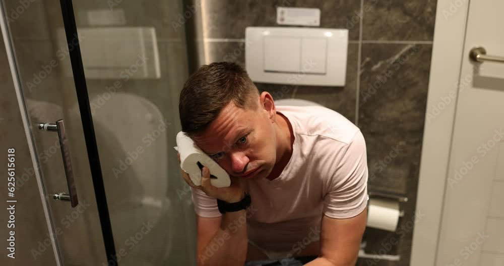 Man applies toilet paper to head sitting on toilet bowl near shower. Concept of daily routine in light bathroom of accommodation slow motion Man applies toilet paper to head sitting on toilet bowl near shower. Concept of daily routine in light bathroom of accommodation slow motion