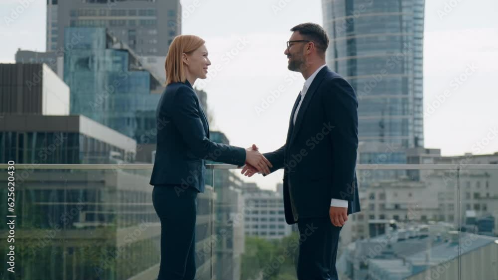 Side view two successful business partners male female handshaking meet and shake hands coming to each other on office building rooftop terrace overlooking high-rise skyscrapers modern city downtown Side view two successful business partners male female handshaking meet and shake hands coming to each other on office building rooftop terrace overlooking high-rise skyscrapers modern city downtown