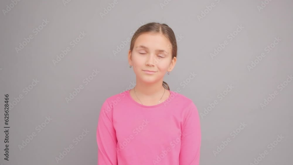 A girl in a pink sweater on a gray background thinks and looks up and to the side. A girl in a pink sweater on a gray background thinks and looks up and to the side.