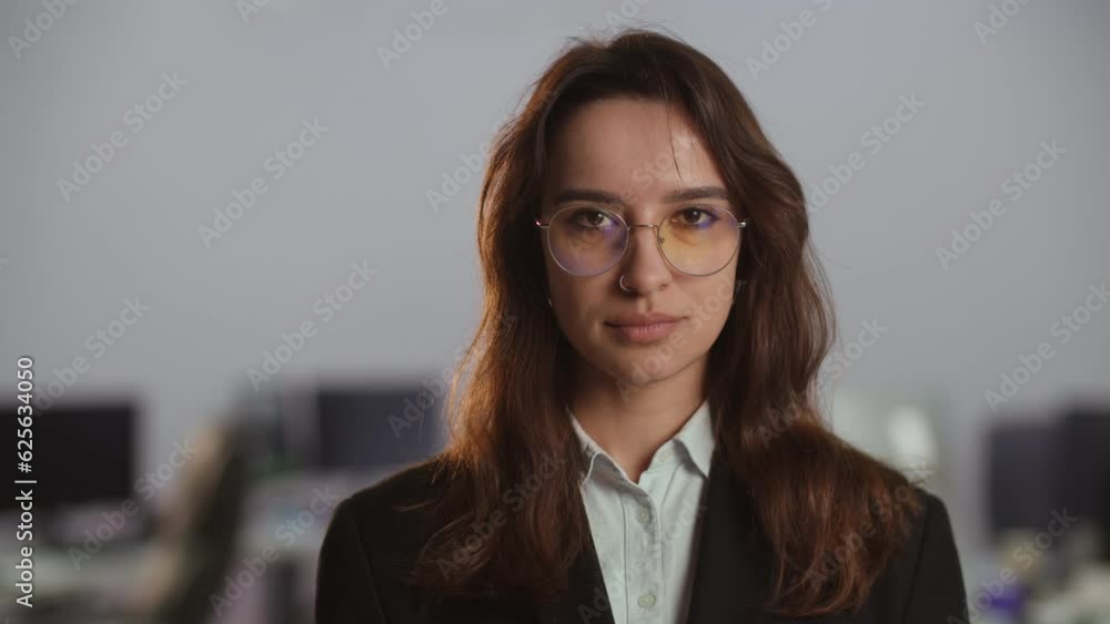 View of smiling businesswoman in glasses and business suit. Close-up shot of a business lady in front of a blurry office background. View of smiling businesswoman in glasses and business suit. Close-up shot of a business lady in front of a blurry office background.