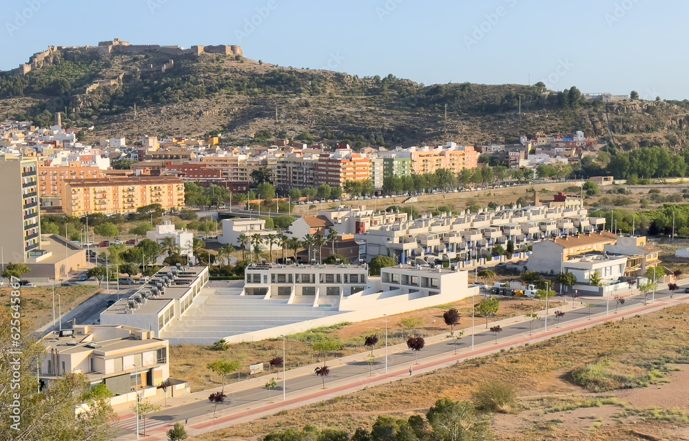 Buildings and houses in city, aerial view. Sagunto Castle on mountain. Ruins walls of Fortress Castle at town of Sagunto. Fortress Castillo in Mountains hills.  Houses roofs in town at mountains.