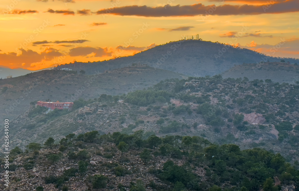 Obraz premium Mountains landscape on sunset. Mountain view from Mola De Segart mountain in Sierra Calderona national park in Valencia, Spain. House in mountains. Landscape of a mountain valley with houses.