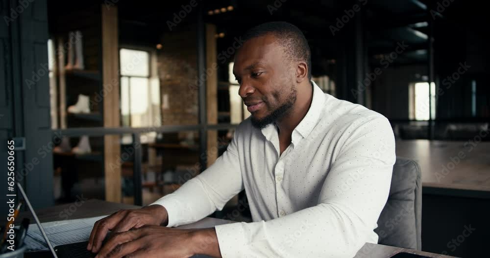 Black-skinned man in a white shirt rejoices at his office work success. An office worker works at a laptop and is very happy for his success Black-skinned man in a white shirt rejoices at his office work success. An office worker works at a laptop and is very happy for his success