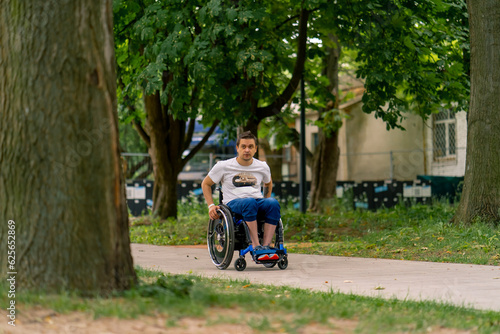 Inclusiveness Portrait of a young man with a disability in a wheelchair in a city park against a background of trees 