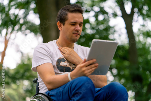 Inclusiveness A man with disabilities in a wheelchair stares intently at the tablet he is holding in the park  © Guys Who Shoot