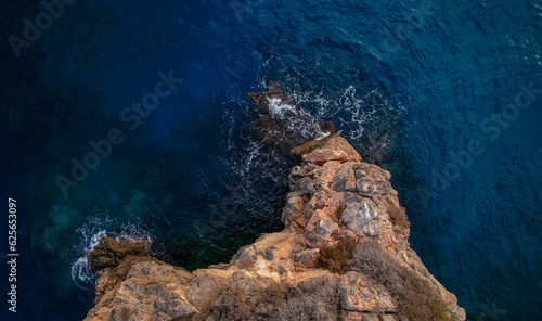 Aerial view of cliffs by the sea. Wave breaking against the rocks. Blue sea with different shades and illuminated rocky cliff at sunset. Granada. Andalusia. Spain.
