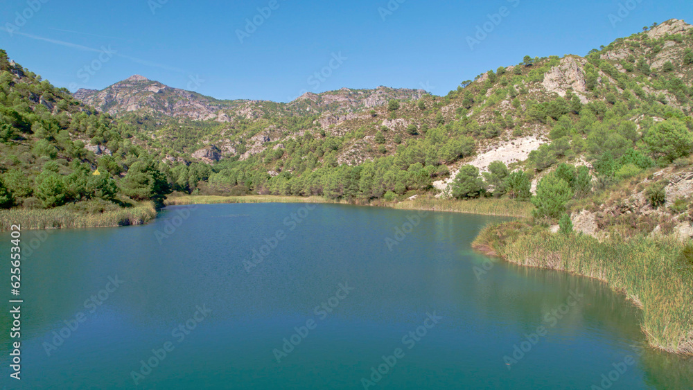 High mountain lagoon next to the forest and mountainous landscape with colorful sky. Aerial view. Los Guajares. Granada. Spain.