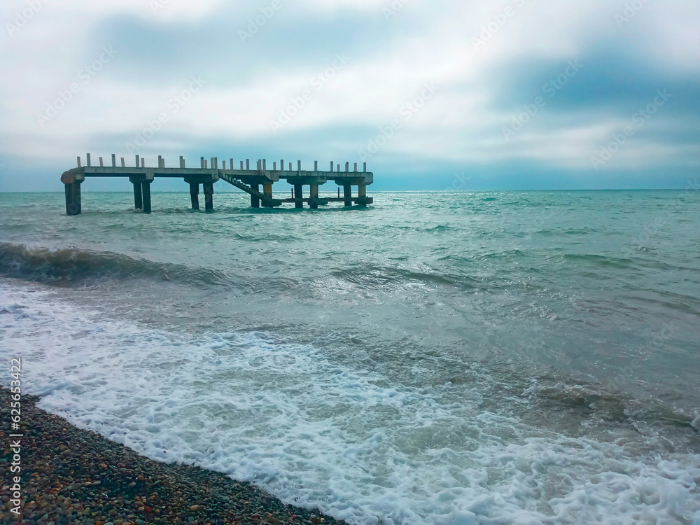 waves on the seashore and a destroyed bridge in the background