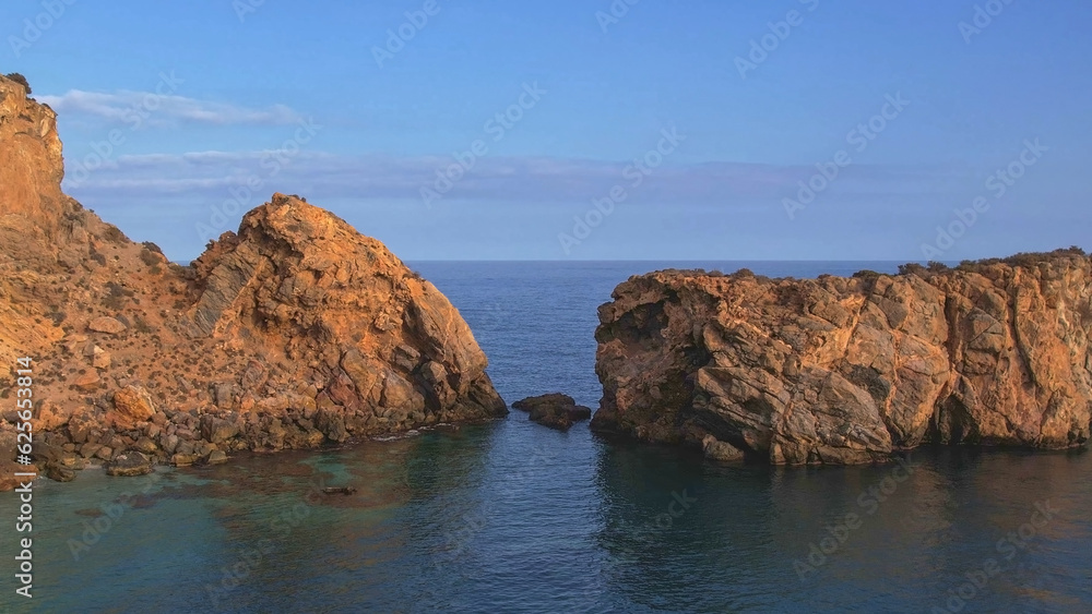 Cliffs and rocky area next to the sea at sunset. Colorful sunset of rocks next to blue sea. Aerial view.
