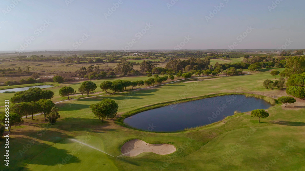 Fairway, sand bunker and lake on golf course at sunset. Spain. Aerial view.