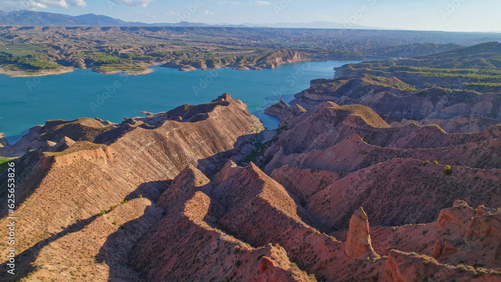 Aerial view over reddish badlands and reservoir at sunset. Panoramic view of ravines and colorful water and coastline. Andalusia. Spain.
