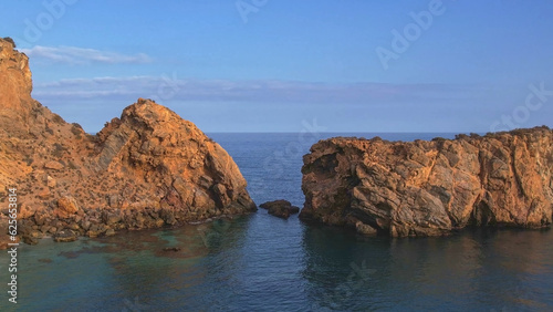 Cliffs and rocky area next to the sea at sunset. Colorful sunset of rocks next to blue sea. Aerial view. 