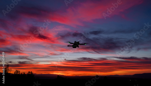 Drone in flight at sunset with colorful sunset. Drone silhouette with position lights at sunset during the golden hour.