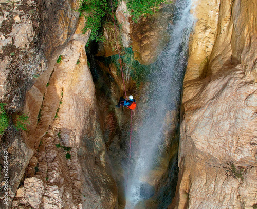 Climber rappelling down a waterfall. Canyoning descent of the waterfall with climbing equipment. Zenith aerial view. Granada. Andalusia. Spain.