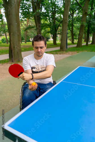 Inclusiveness A disabled man in a wheelchair plays ping pong in a city park against a backdrop of trees  © Guys Who Shoot