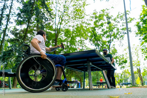 Inclusiveness A disabled man in a wheelchair plays ping pong against an old man with a gray beard in a city park 