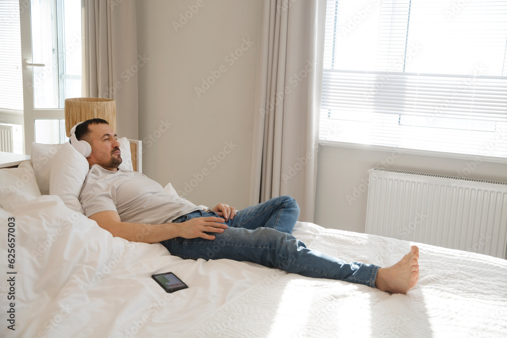 man wearing headphones with mobile phone relaxed on the bed of your apartment. concept without stress. mental health. work from vacation home man wearing headphones with mobile phone relaxed on the bed of your apartment. concept without stress. mental health. work from vacation home