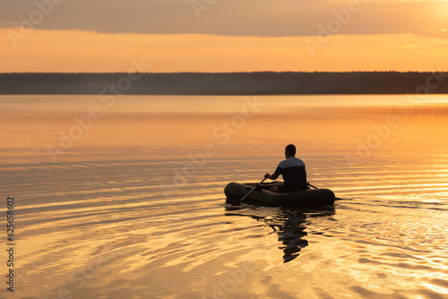A man is floating on a lake on an inflatable boat in the sunset light