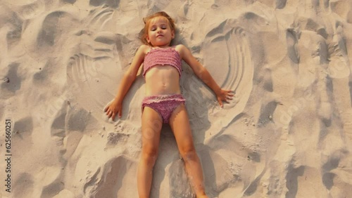 A child playing in a brown swimsuit lying on the beach on the sand makes an snow angel