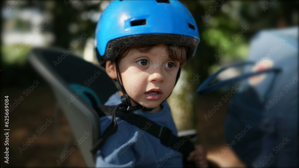 Child wearing helmet in bicycle back seat riding bike with parent Child wearing helmet in bicycle back seat riding bike with parent