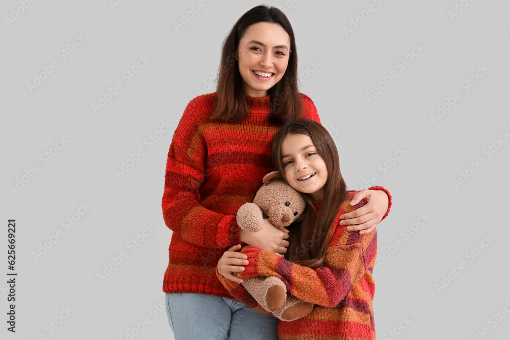 Little girl and her mother in warm sweaters with toy bear on grey background Little girl and her mother in warm sweaters with toy bear on grey background