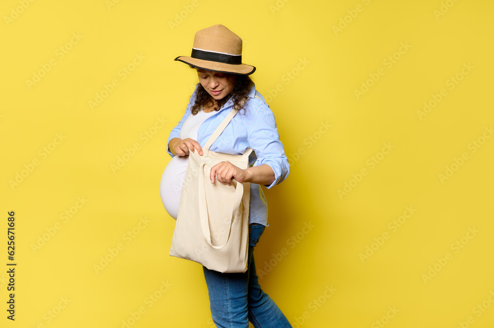 Charming pregnant woman using linen shopping bag, isolated yellow background with copy ad space. Sustainable lifestyle Charming pregnant woman using linen shopping bag, isolated yellow background with copy ad space. Sustainable lifestyle