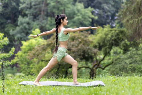 Young beautiful woman in the park on a sports mat doing fitness and doing active sports exercises, Hindu woman doing yoga in the park in the morning among the trees, stretching and meditating