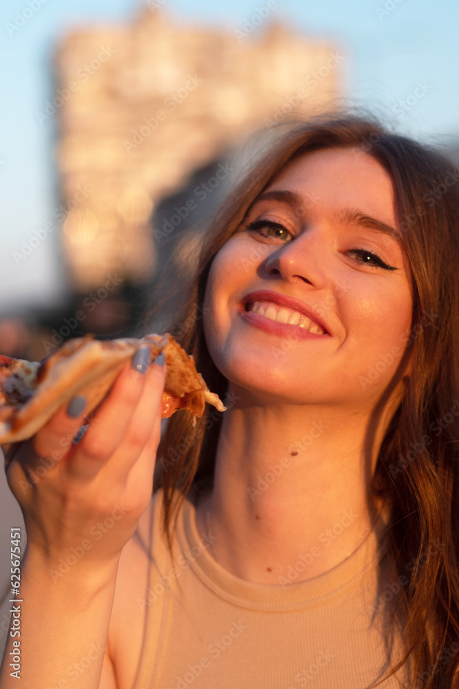 portrait of a woman eating a slice of pizza and smiles