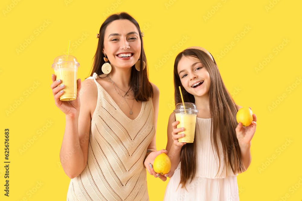 Little girl with her mother drinking lemon smoothie on yellow background Little girl with her mother drinking lemon smoothie on yellow background