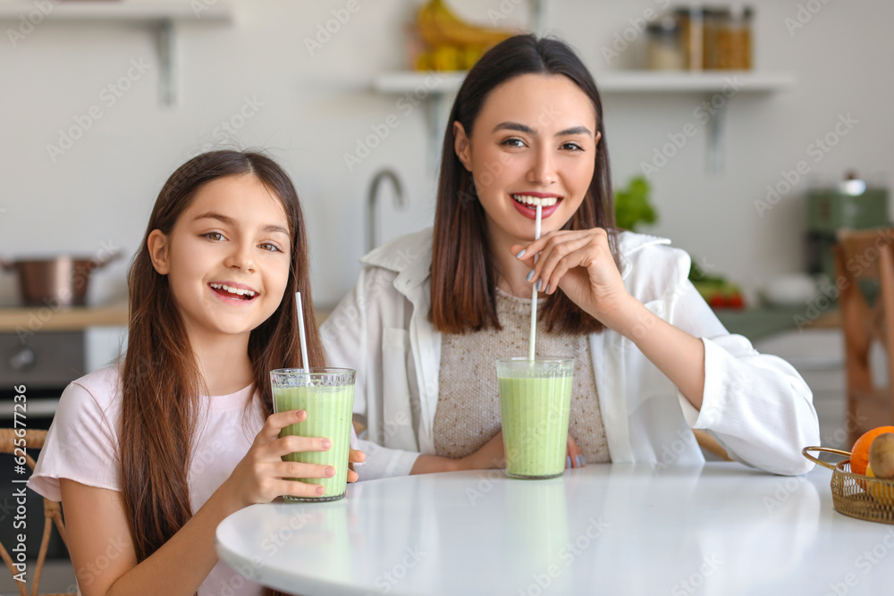 Little girl with her mother drinking green smoothie at table in kitchen Little girl with her mother drinking green smoothie at table in kitchen