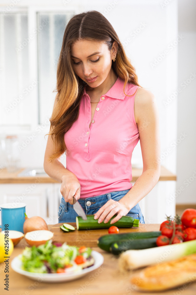 Smiling young woman preparing vegetable salad in home kitchen