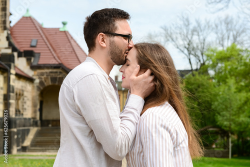 Young man kissing his girlfriend on her forehead in park