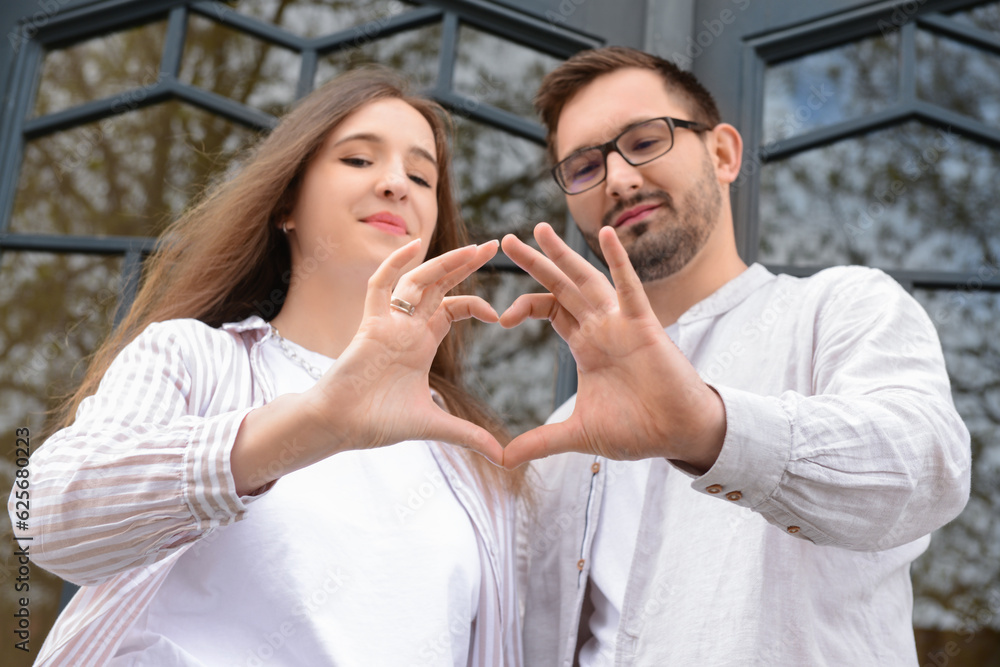 Beautiful happy couple making heart shape with their hands in city Beautiful happy couple making heart shape with their hands in city