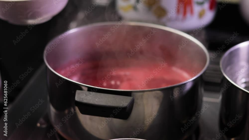 Skimming the foam off of raspberry jam while cooking in a pot on a