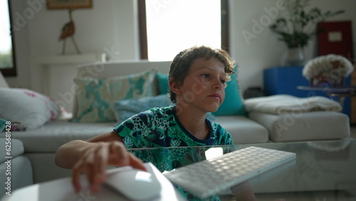 Tired little boy yawning browsing internet online using mouse and keyboard