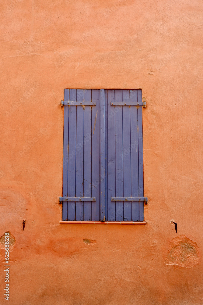Obraz premium Closed vintage window of blue colour with old wooden shutters on the vibrant orange wall. Elegant retro architectural details