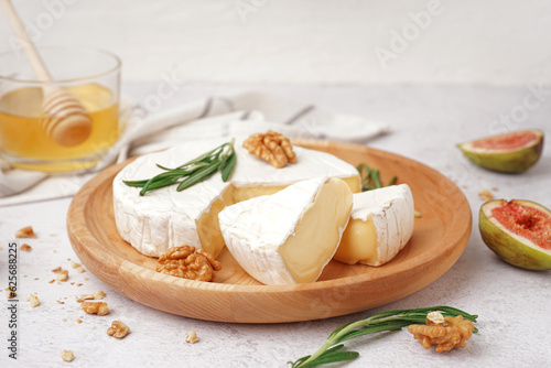 Quadro su tela Plate with pieces of tasty Camembert cheese on light background