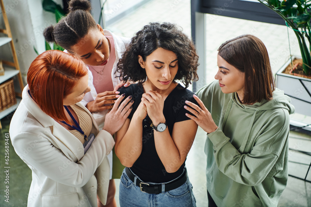 high angle view of psychologist and multiethnic female friends calming frustrated multiracial woman standing with closed eyes in consulting room, moral support and mental wellness concept high angle view of psychologist and multiethnic female friends calming frustrated multiracial woman standing with closed eyes in consulting room, moral support and mental wellness concept