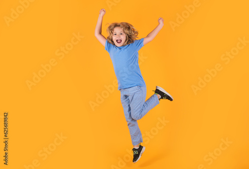 Funny boy jumping in air. Boy jumping. Full size of kid boy have fun jump up isolated over yellow background.