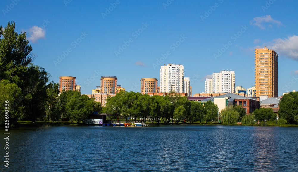 Beautiful panoramic landscape - modern high-rise buildings on the shore of a pond among the lush foliage of trees in Reutov, Moscow region on a clear summer sunny day