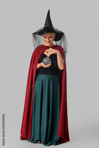Mature witch with crystal ball on grey background